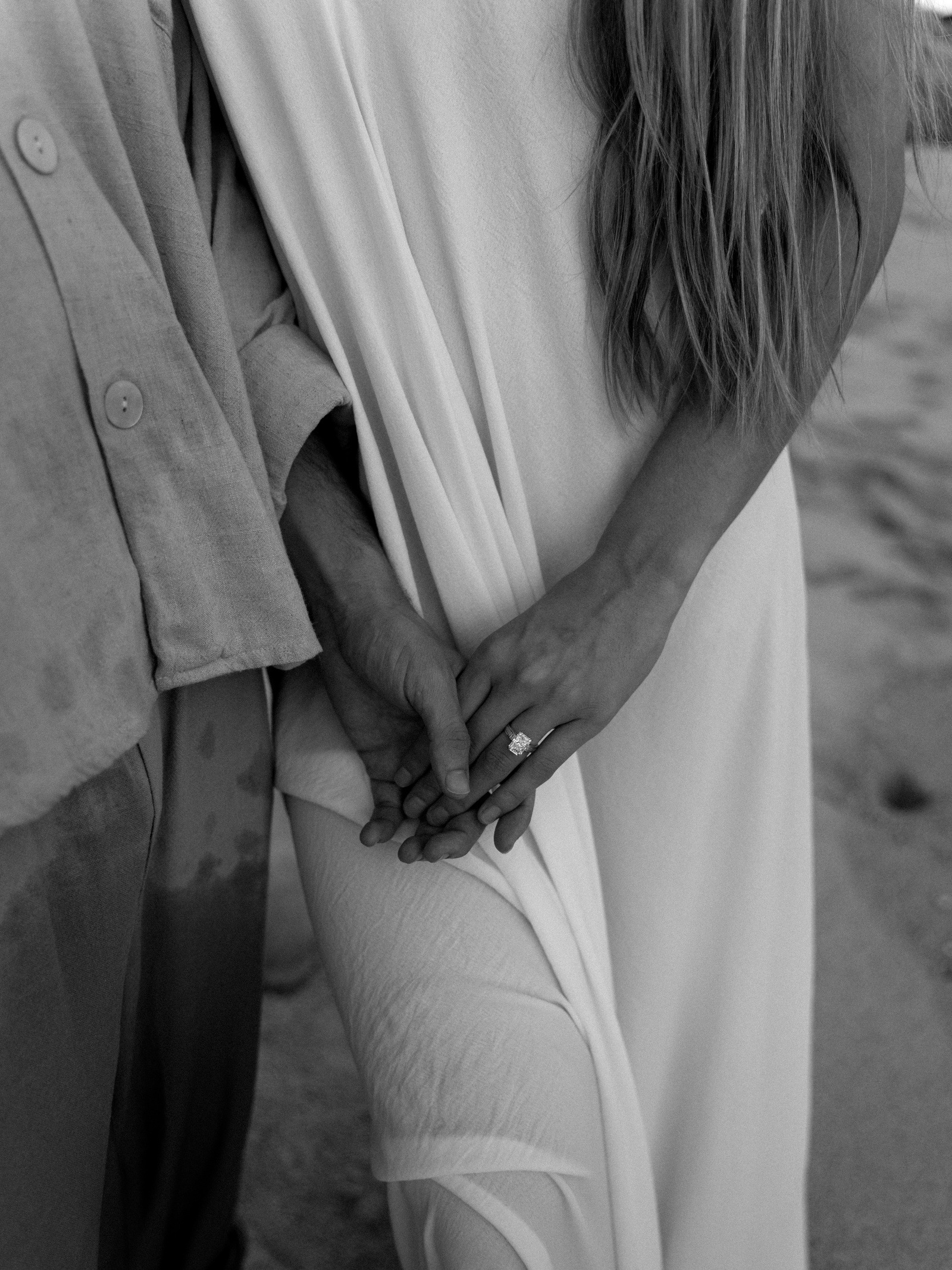 An engagement ring and intertwined hands in black and white