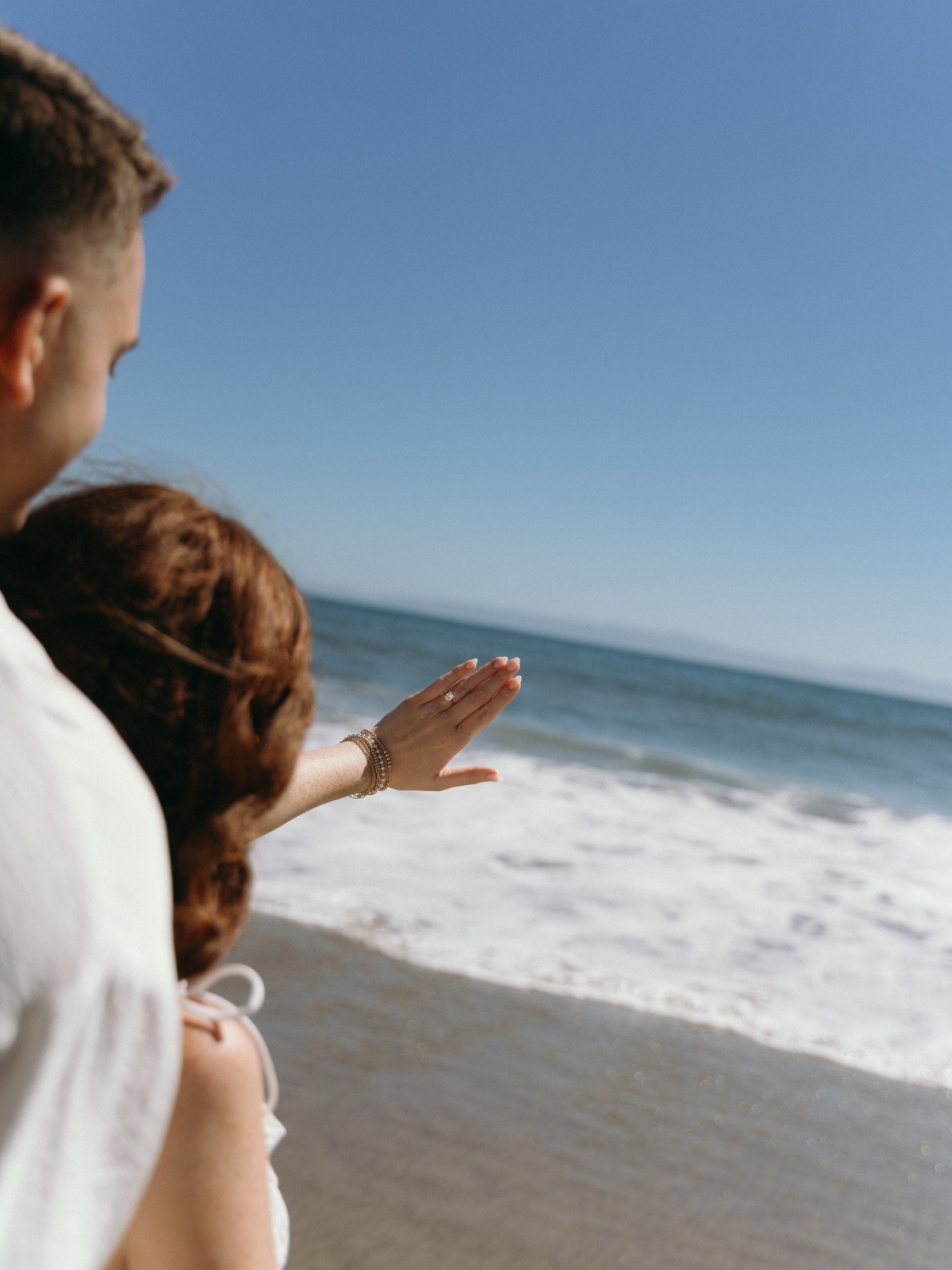 An engagement ring held up against the ocean