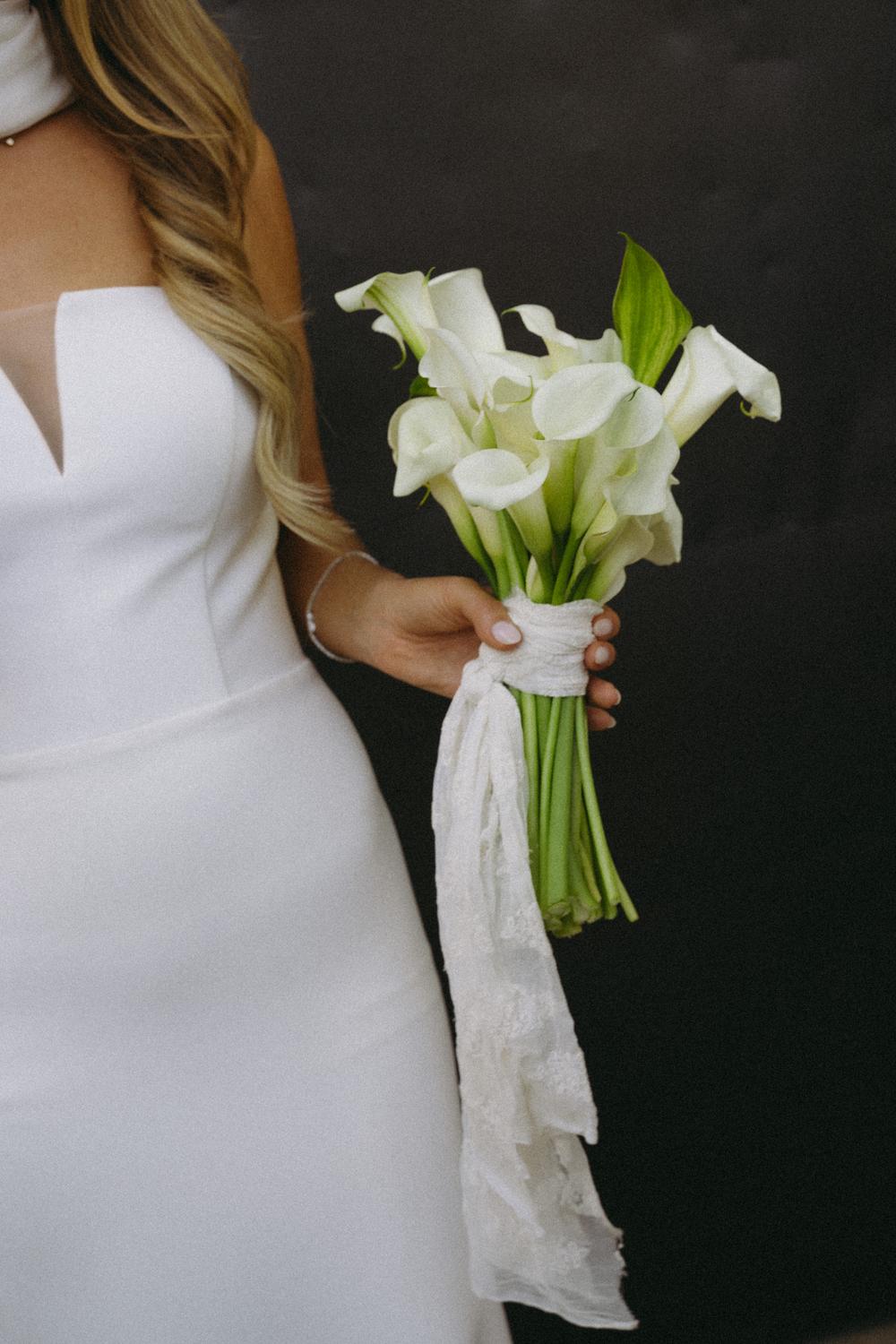 White calla lilies held beside a bridal dress