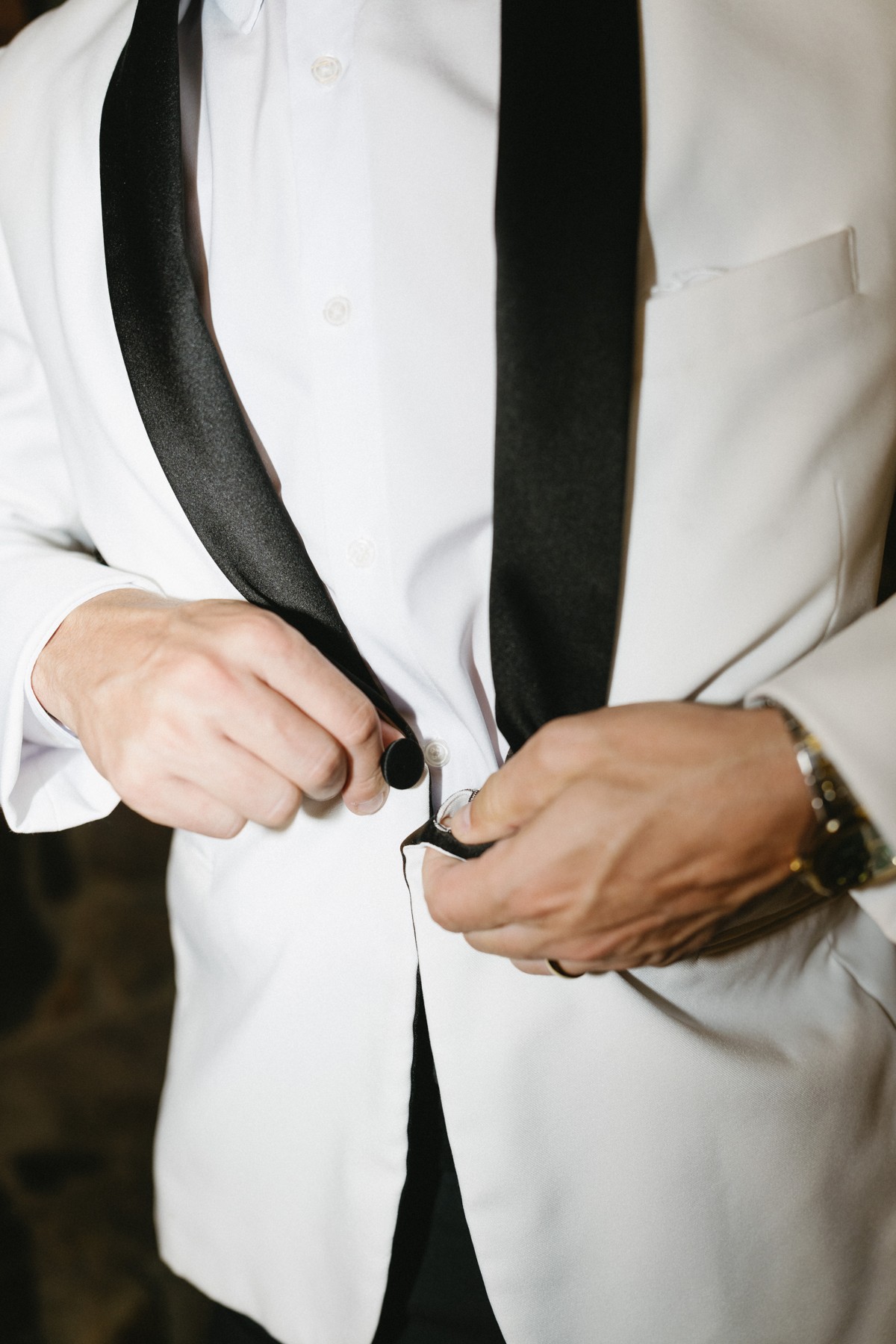 The groom fastening his white dinner jacket