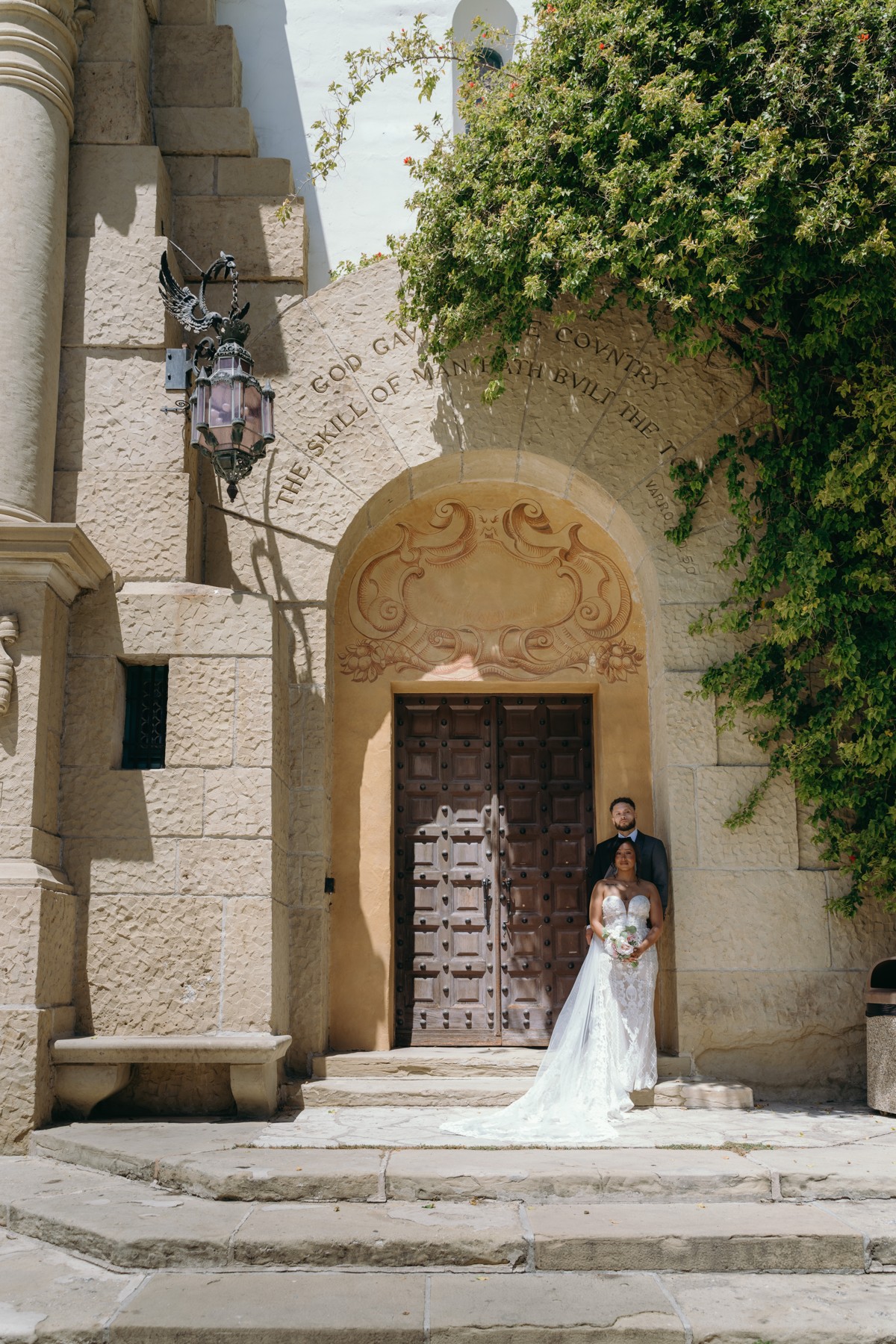 A wedding couple beneath a stone archway framed by greenery
